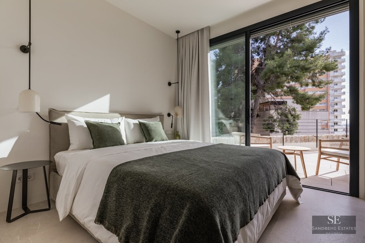 Bright bedroom featuring a double bed with green accents and large glass sliding doors opening to a terrace.