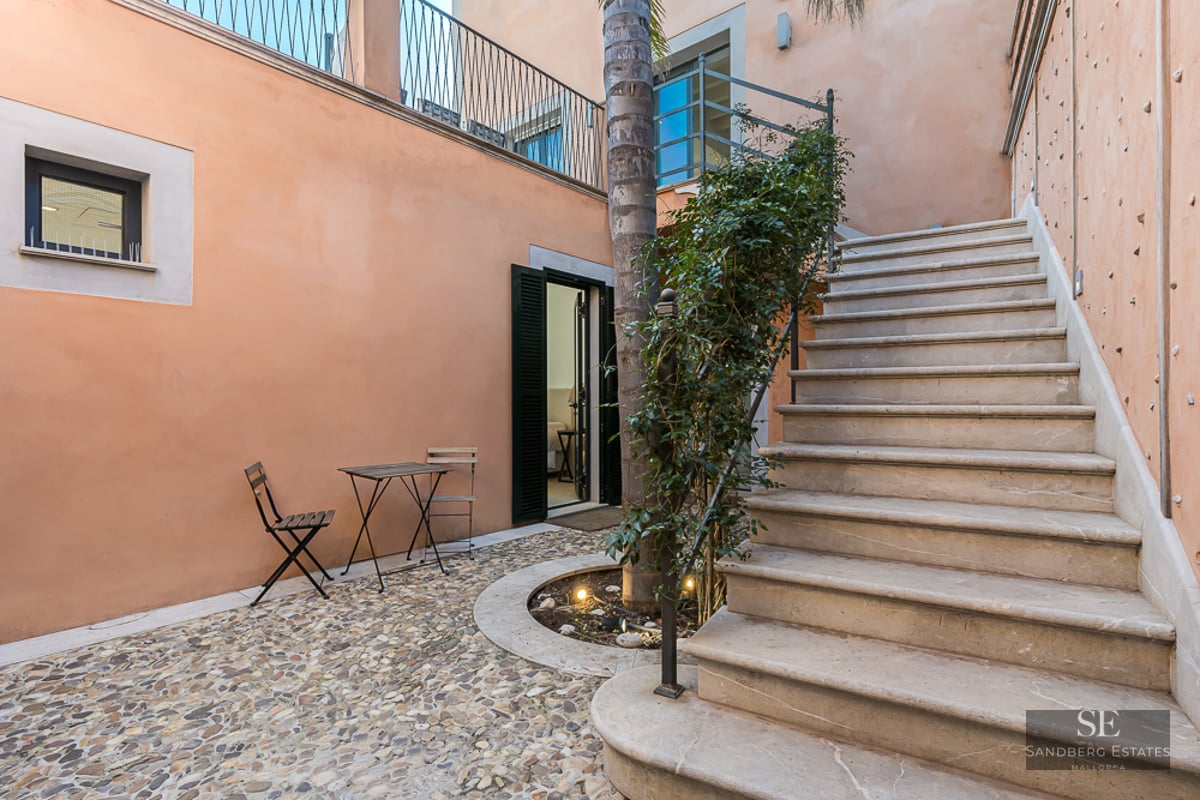 Private peach-walled courtyard with a pebble floor, a stone staircase, and a small bistro table with chairs.