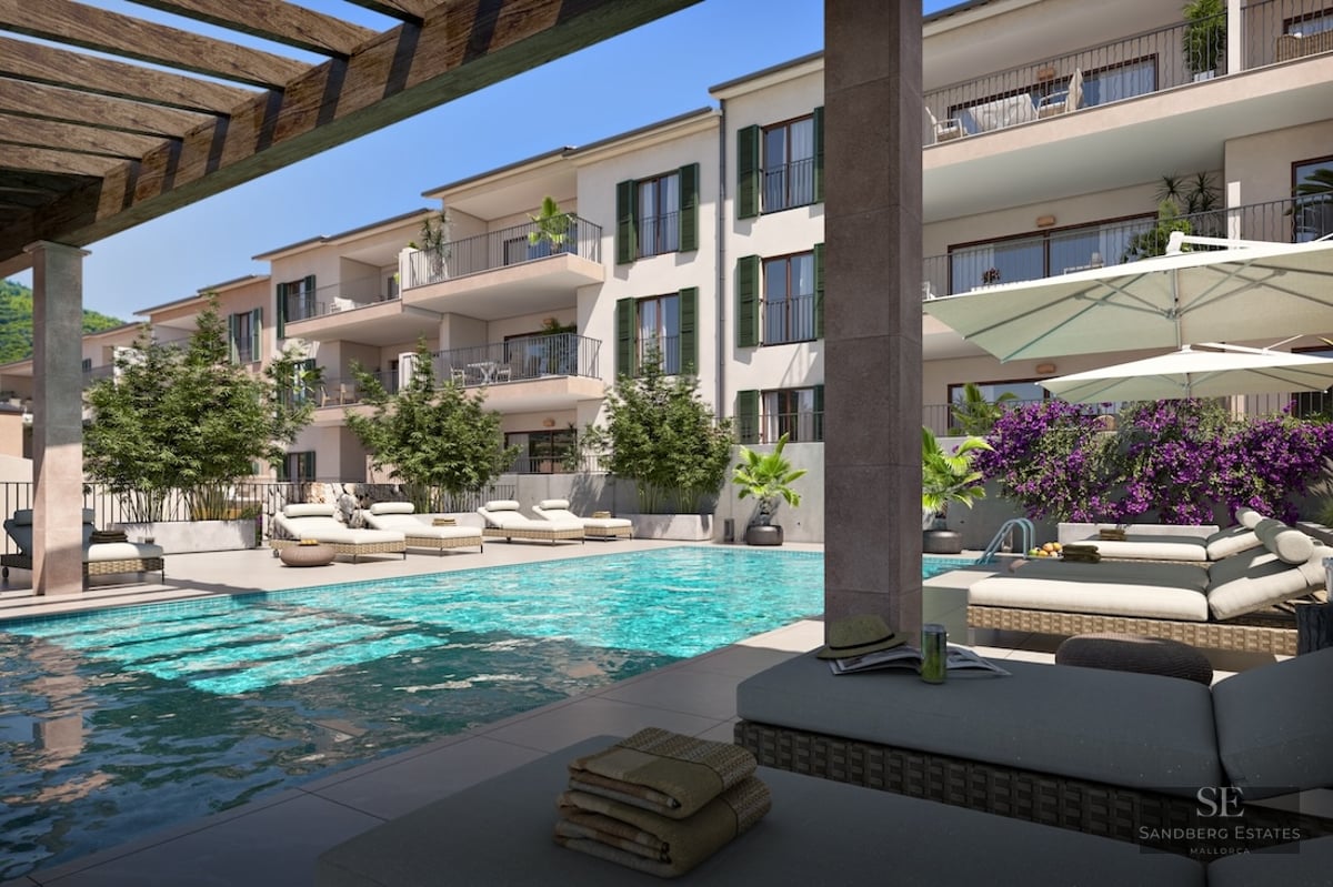 Modern turquoise pool area with sun loungers, umbrellas, and a wooden pergola next to a Mediterranean-style building.