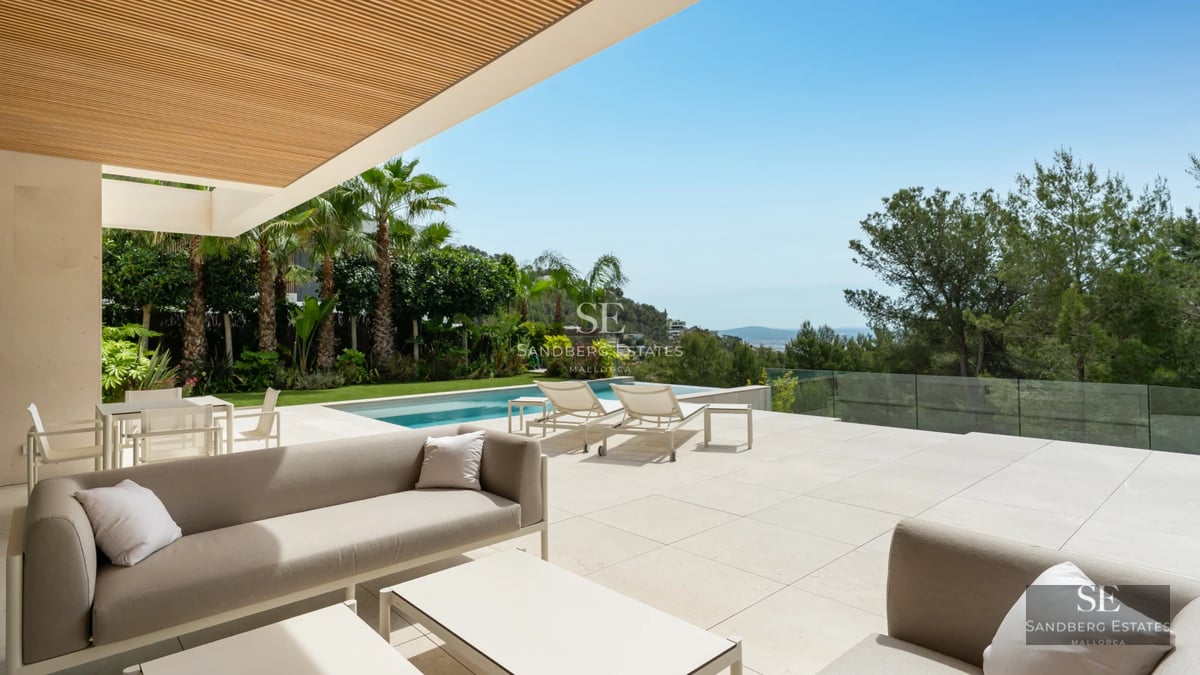 Panoramic view of modern villa with infinity pool and expansive terraces. Sleek and minimalist architecture. Blue sky and lush vegetation.