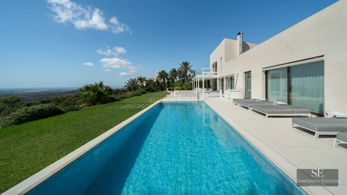 Pool view featuring sun loungers, palm trees, and a modern design house with large windows. Luxurious and minimalist exterior.