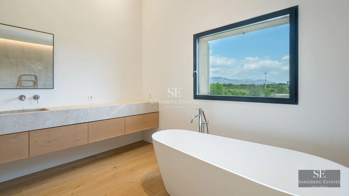 Spacious living room with floor-to-ceiling windows, natural light, wood floors, modern fireplace, and elegant decor. View of lush garden.