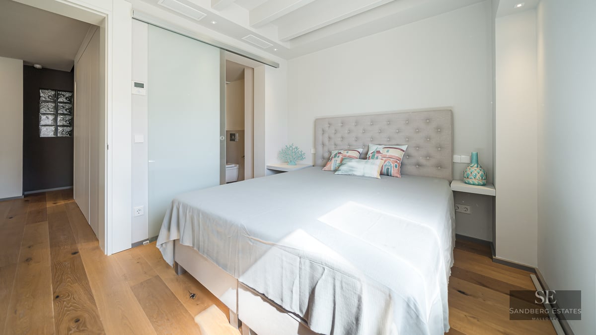Bright bedroom featuring a bed with a tufted headboard, wood floors, and a frosted glass sliding door to a bathroom.