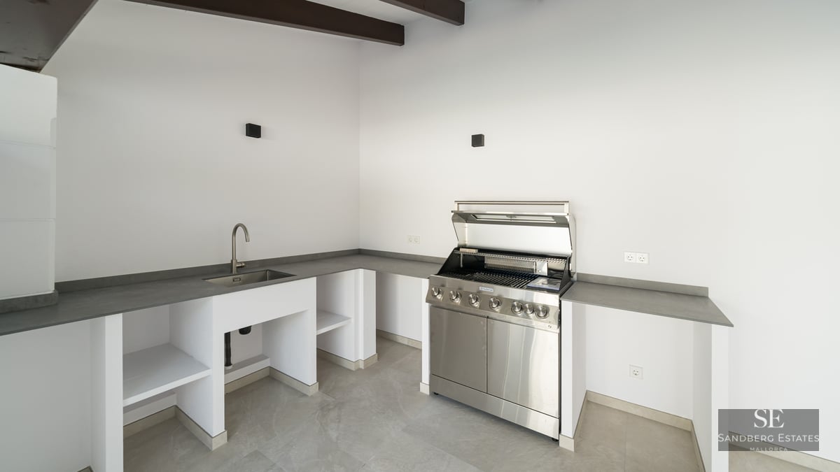 Contemporary outdoor kitchen featuring a stainless steel grill, integrated sink, and sleek gray countertops.