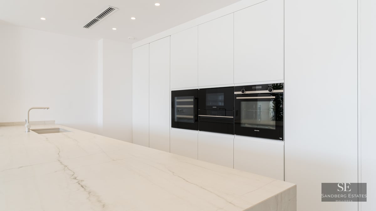 Modern white kitchen featuring a large marble island, integrated sink, and Siemens built-in appliances in handle-less cabinetry.