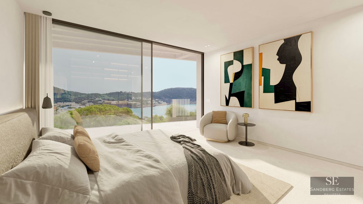 Modern master bedroom with large glass doors overlooking a coastal landscape, featuring abstract art and a lounge chair.