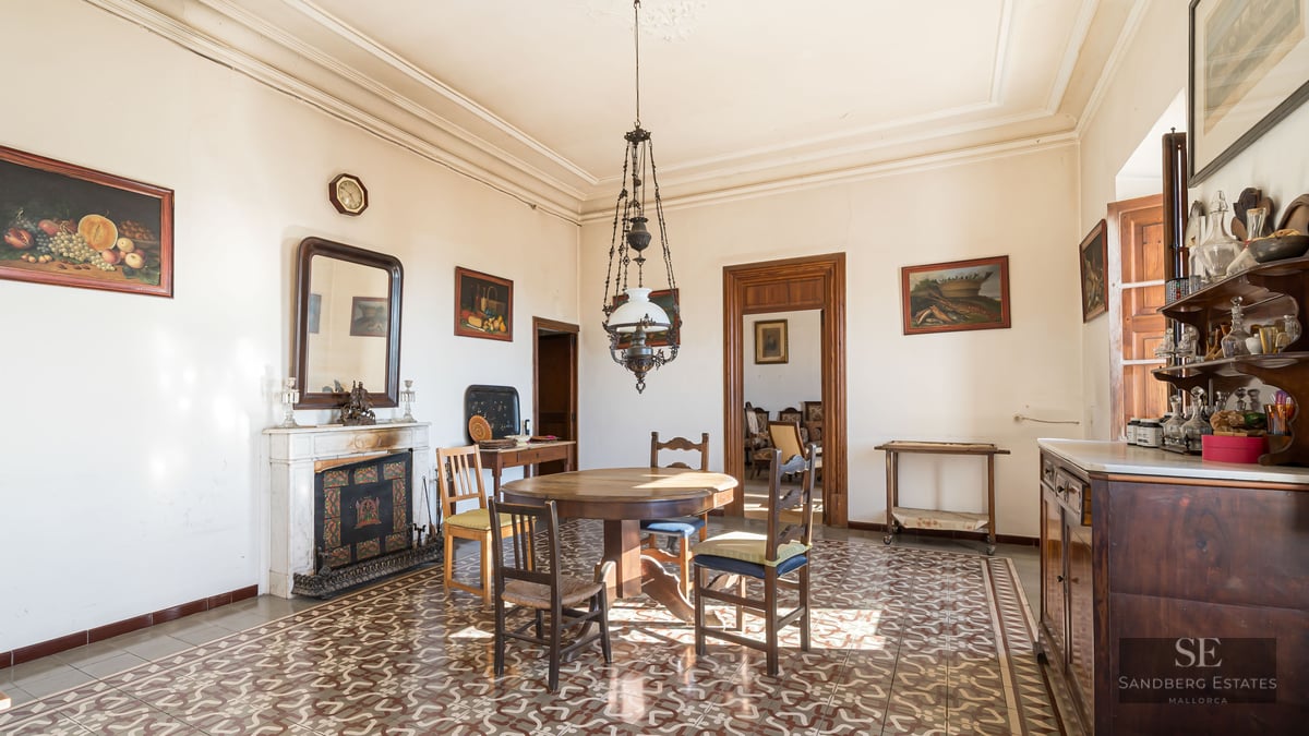 Antique dining room with wooden table, ornate floor tiles, marble fireplace, and high ceilings.