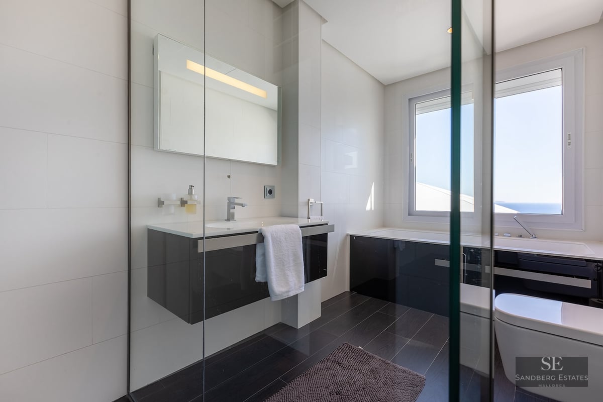 Modern bathroom with white tiled walls, dark floors, a floating vanity, and a bathtub under a large window.