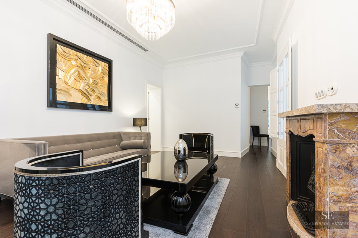 Luxury living room with grey velvet sofa, black table, marble fireplace, and gold wall art.
