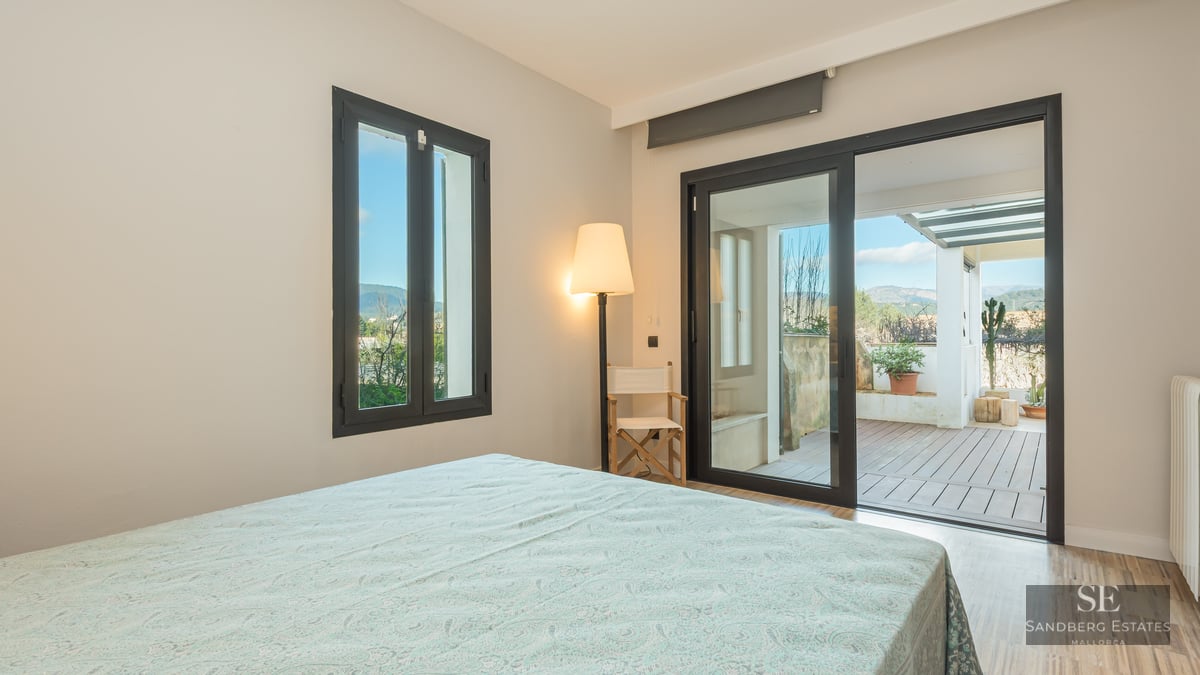 Bright bedroom with sliding glass doors opening to a wood-decked terrace with mountain views.