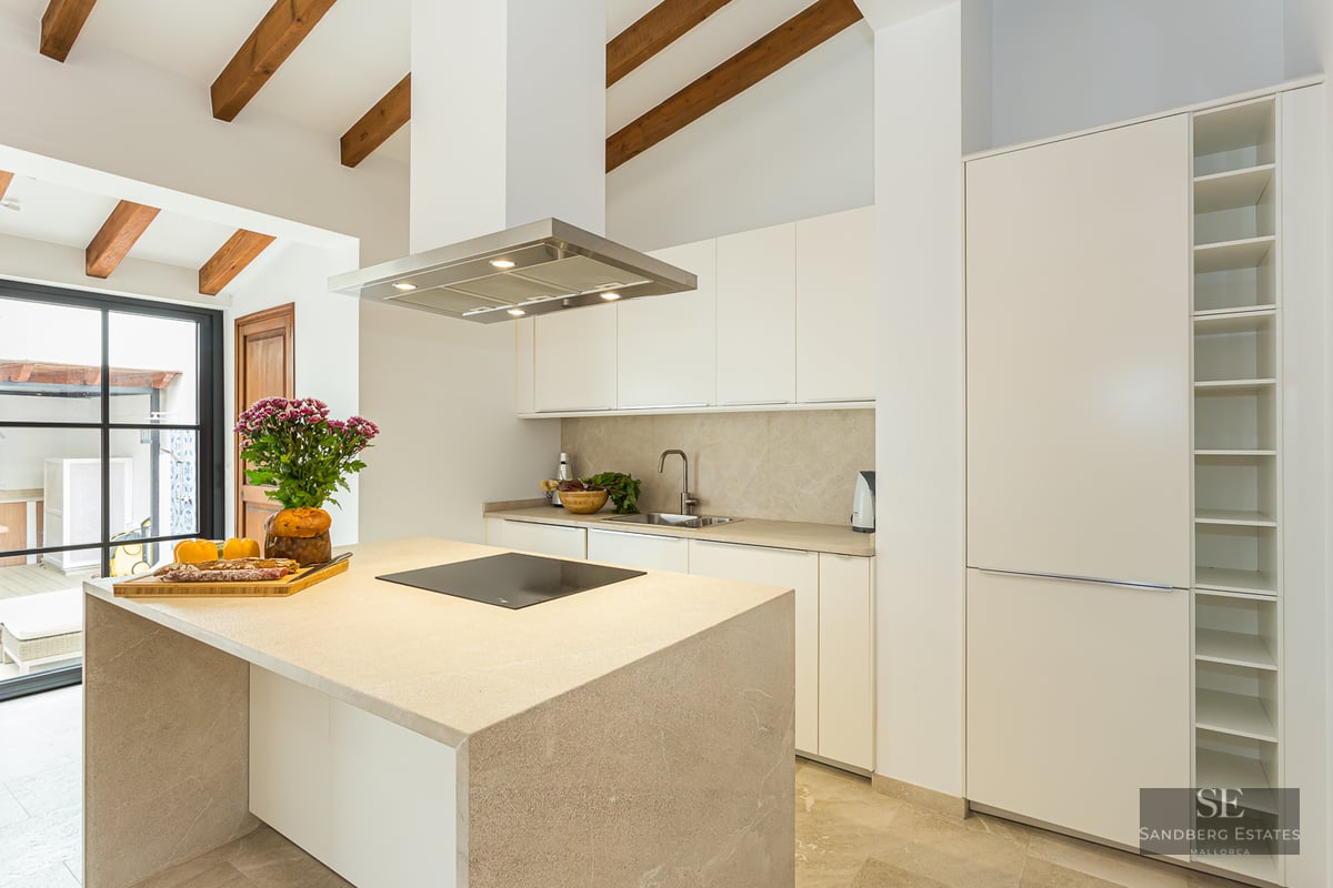 Bright kitchen featuring a stone island, exposed wooden ceiling beams, and minimalist white cabinetry.