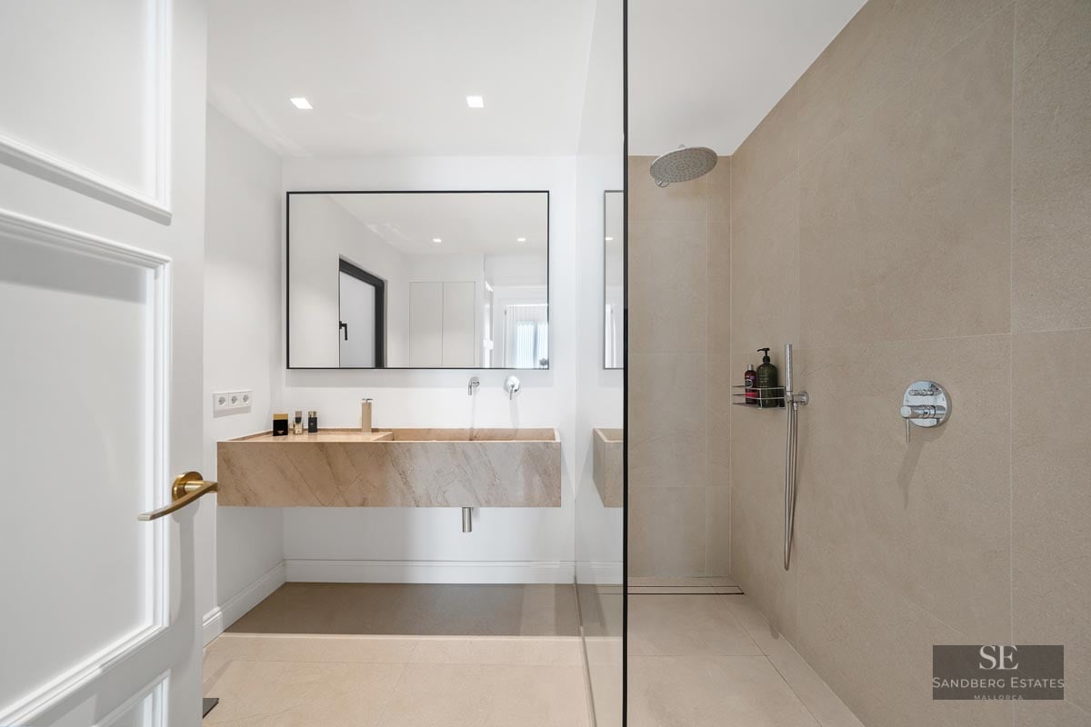 Modern bathroom featuring a floating stone vanity, large mirror, and a walk-in glass shower with beige tiles.