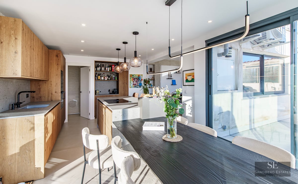 Modern kitchen with stone island and black wooden dining table with cream bouclé chairs.
