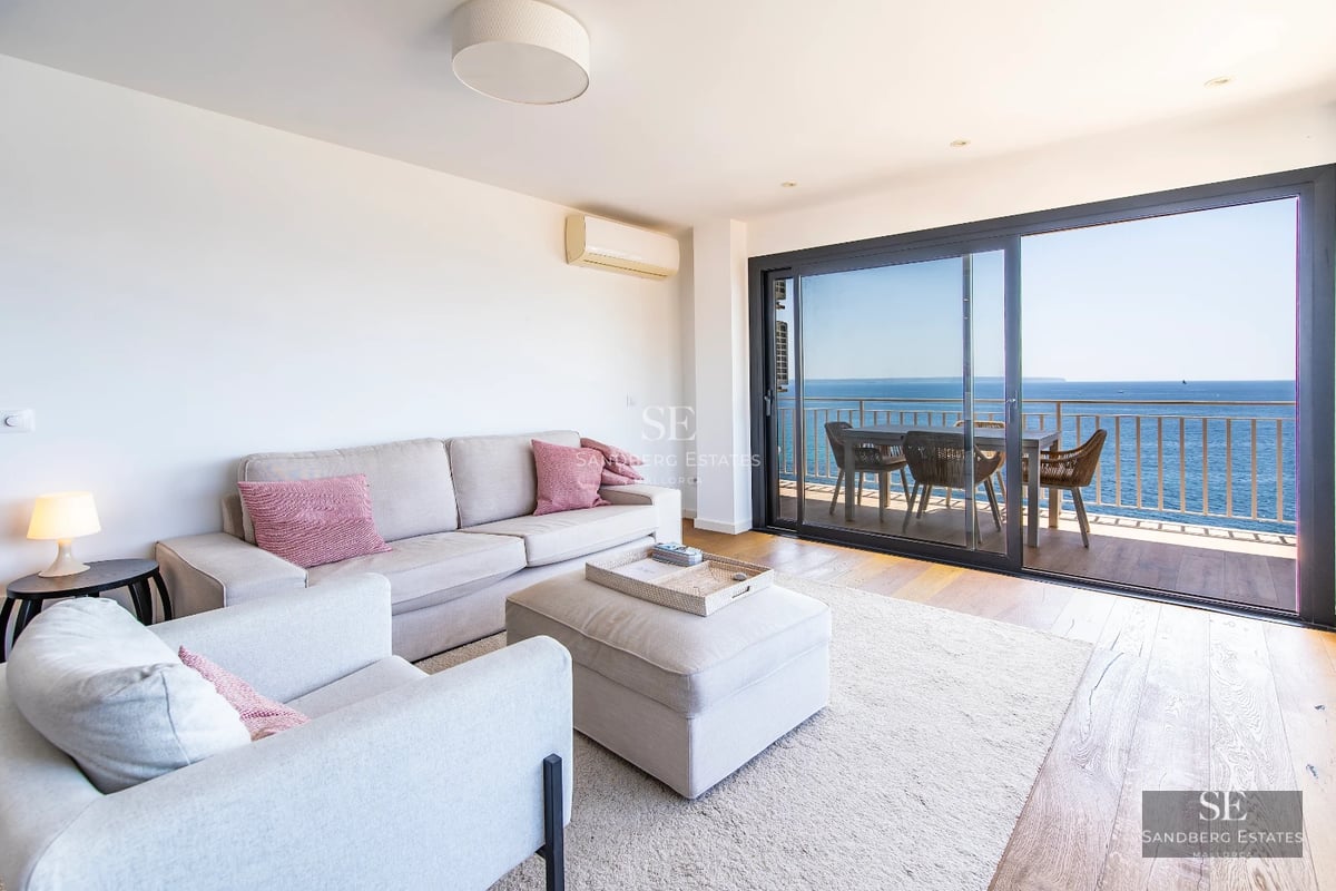 Bright modern interior with sea views. Balcony with glass railing, stylish furniture, and a pool visible outside.