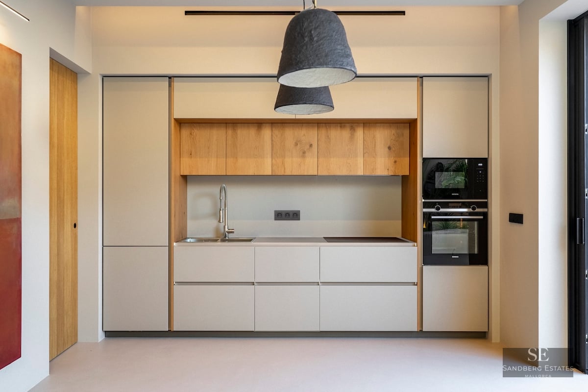 Cuisine moderne aux meubles crème, détails en chêne, appareils intégrés et grandes suspensions texturées.