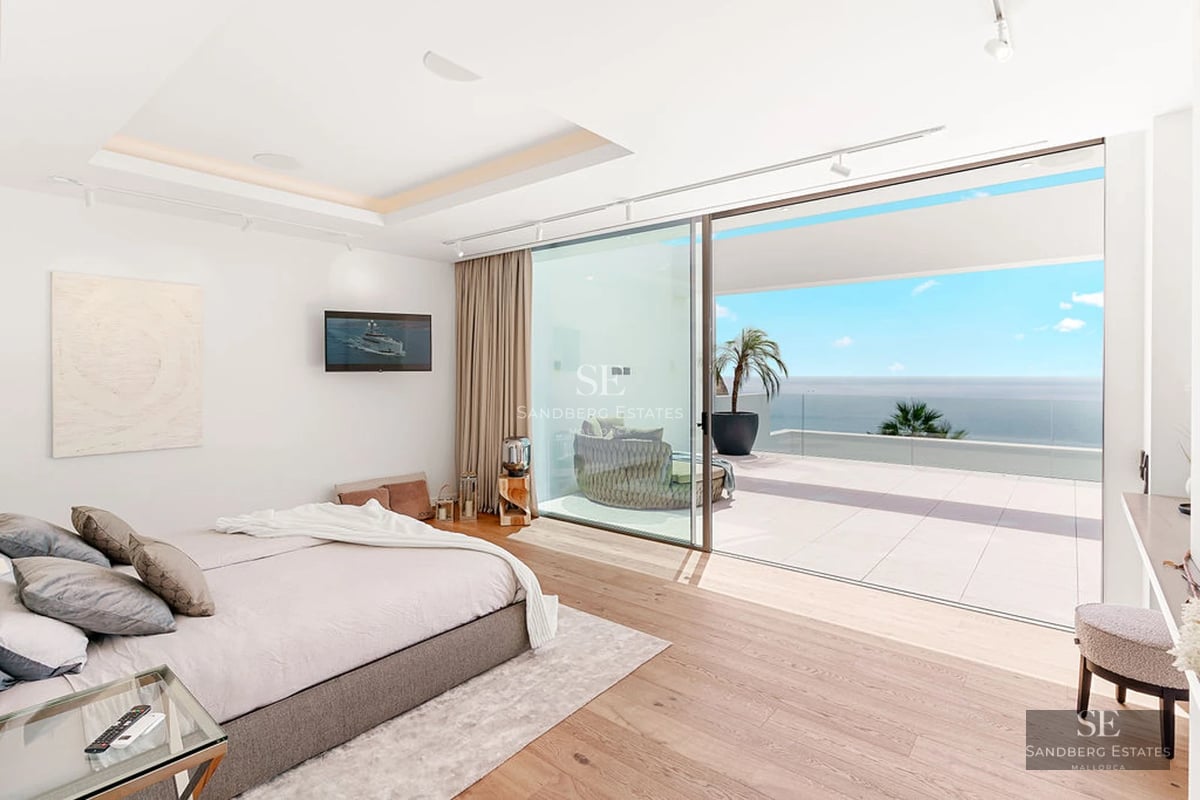 View of reflecting pool bordered by green grass. Lounge chairs, umbrellas, plants. Modern house in the background.