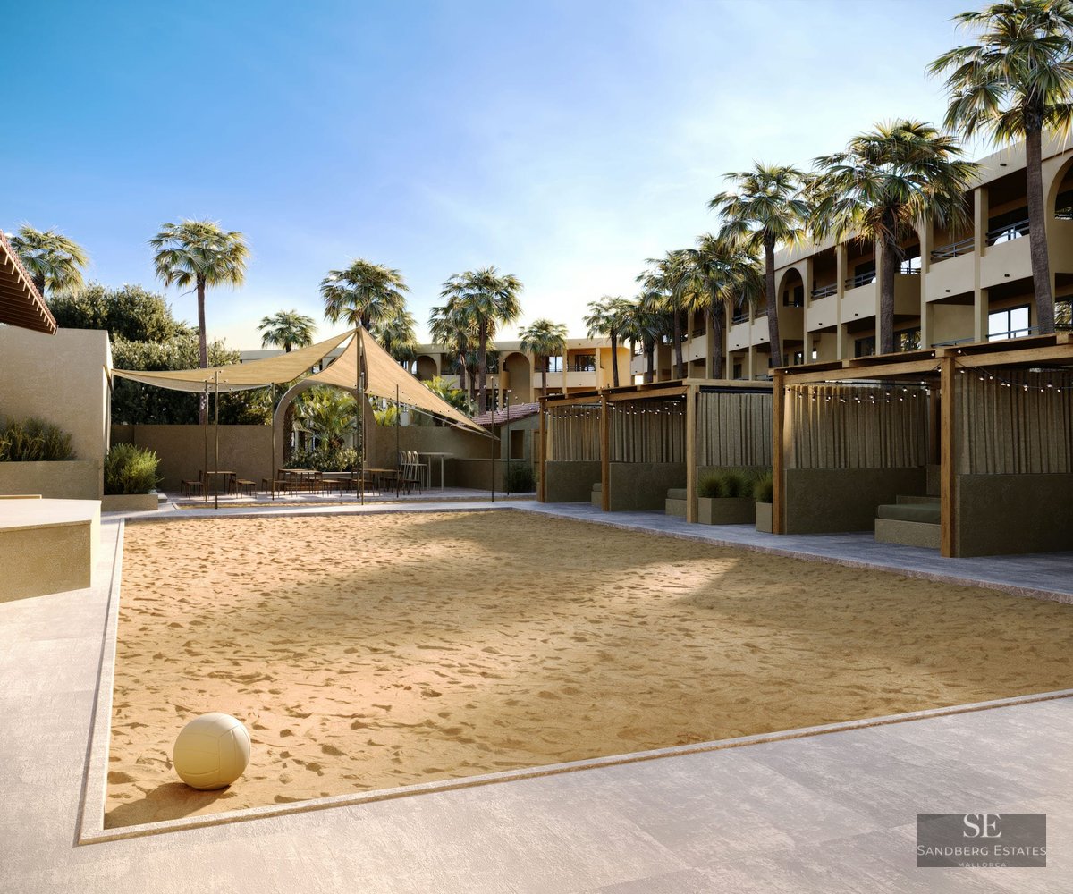Terrain de volley-ball en sable avec un ballon au premier plan, entouré de cabanes en bois, de palmiers et de voiles d'ombrage.