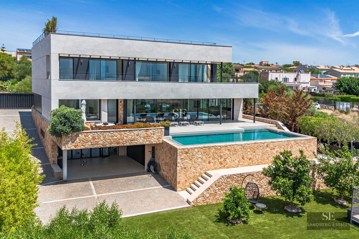 Spacious, bright living room with large windows, light wood floor, and modern furniture. Garden view with pool.