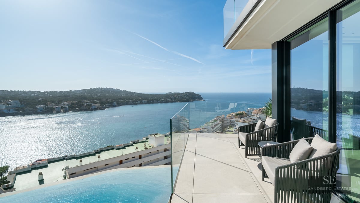 Modern terrace with designer chairs, glass railing, and views over a blue bay and infinity pool.
