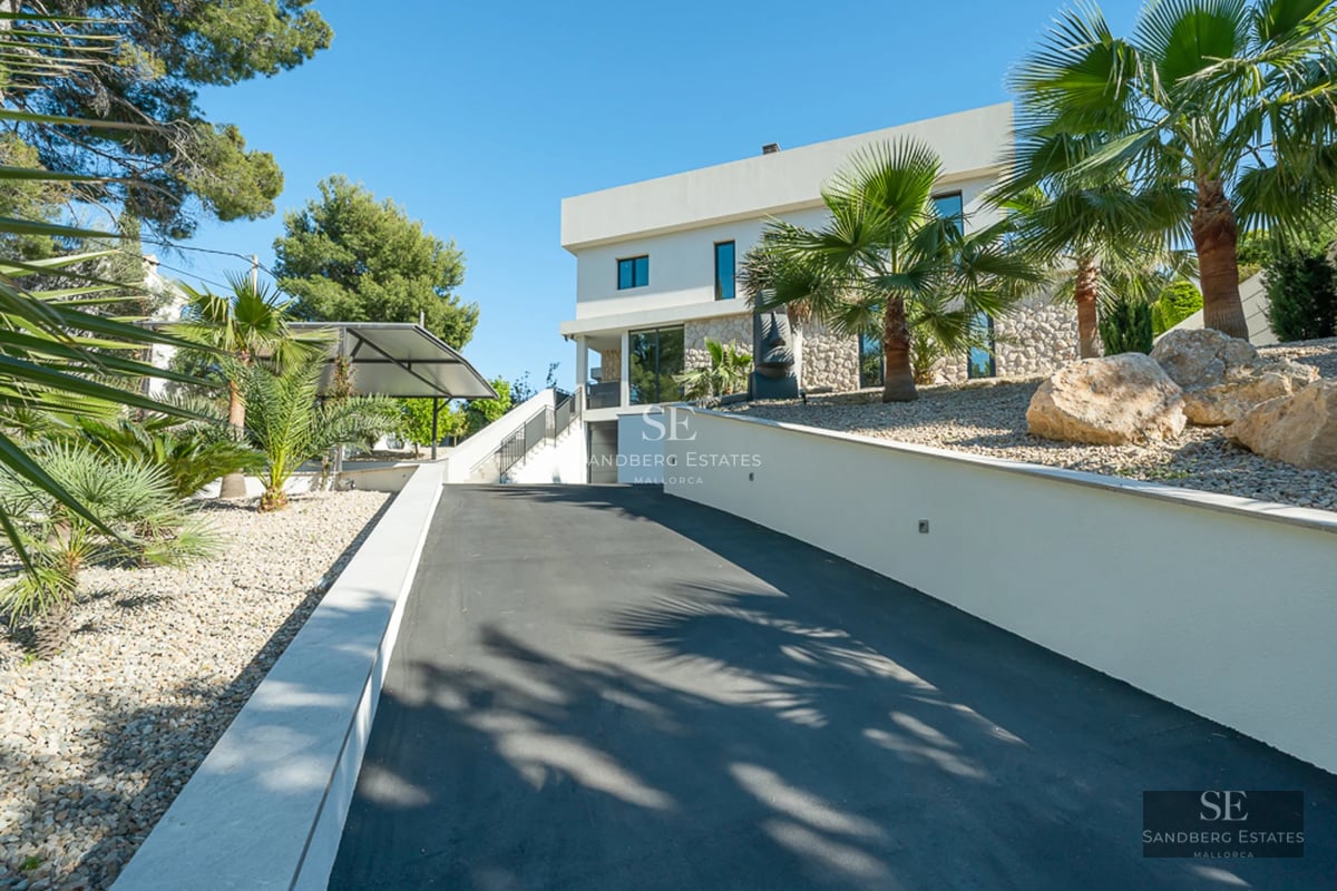 Large swimming pool with sun loungers, green garden, and modern facade of a detached house with large windows. Clear blue sky.