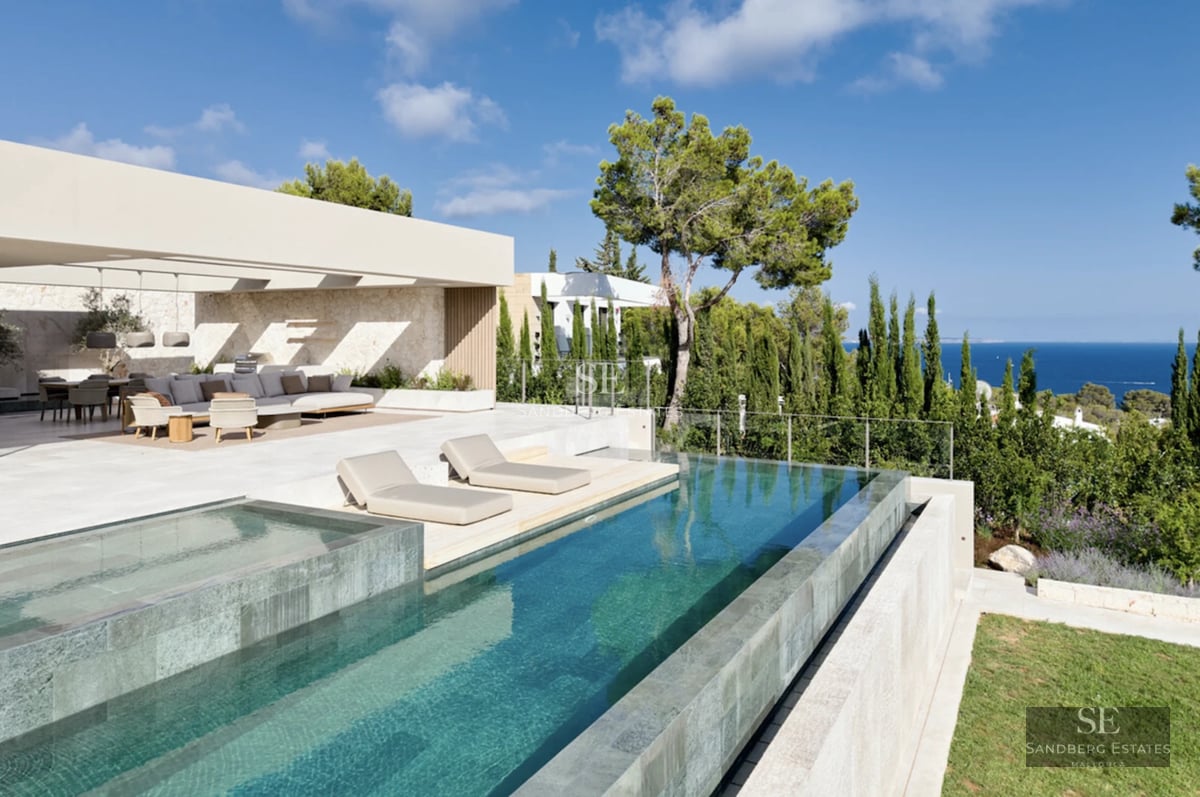 Large pool with sun loungers, surrounded by gardens and a modern luxury villa with large windows and balconies. Minimalist design.