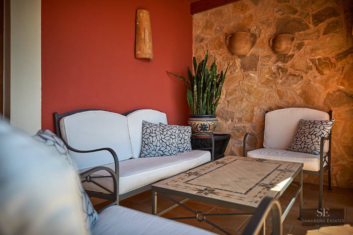 A terrace with white sofas, a mosaic table, a natural stone wall, and a vibrant red accent wall.