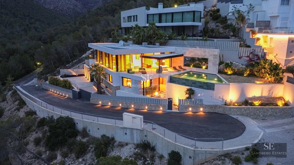 View of a luxurious villa with infinity pool, landscaped gardens, and modern architecture. Stone facade and large windows.