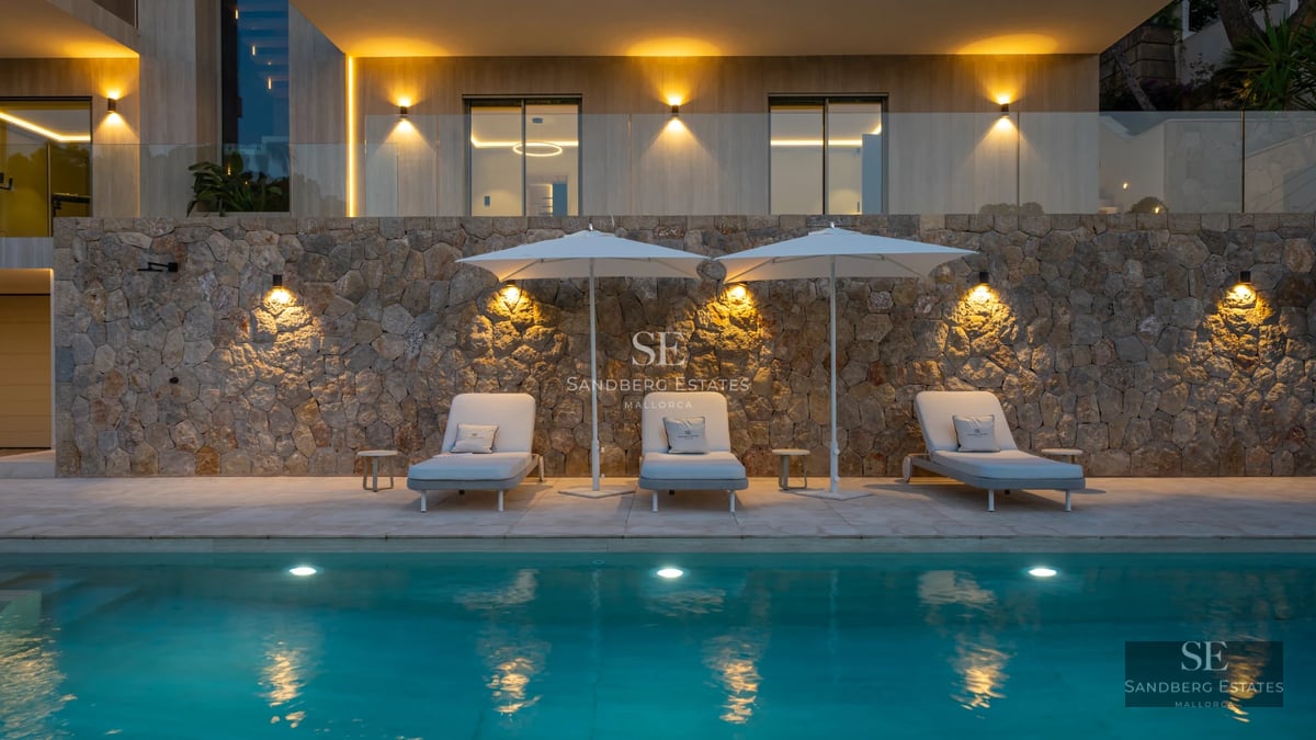 View of a luxurious pool surrounded by manicured garden. Modern design, stylish sun loungers and lush green vegetation.