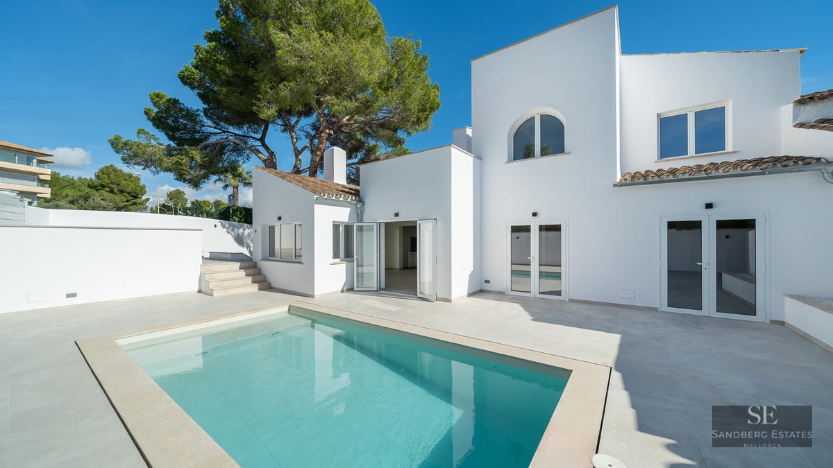Modern white villa featuring a rectangular swimming pool and sun-drenched terrace under a clear blue sky.
