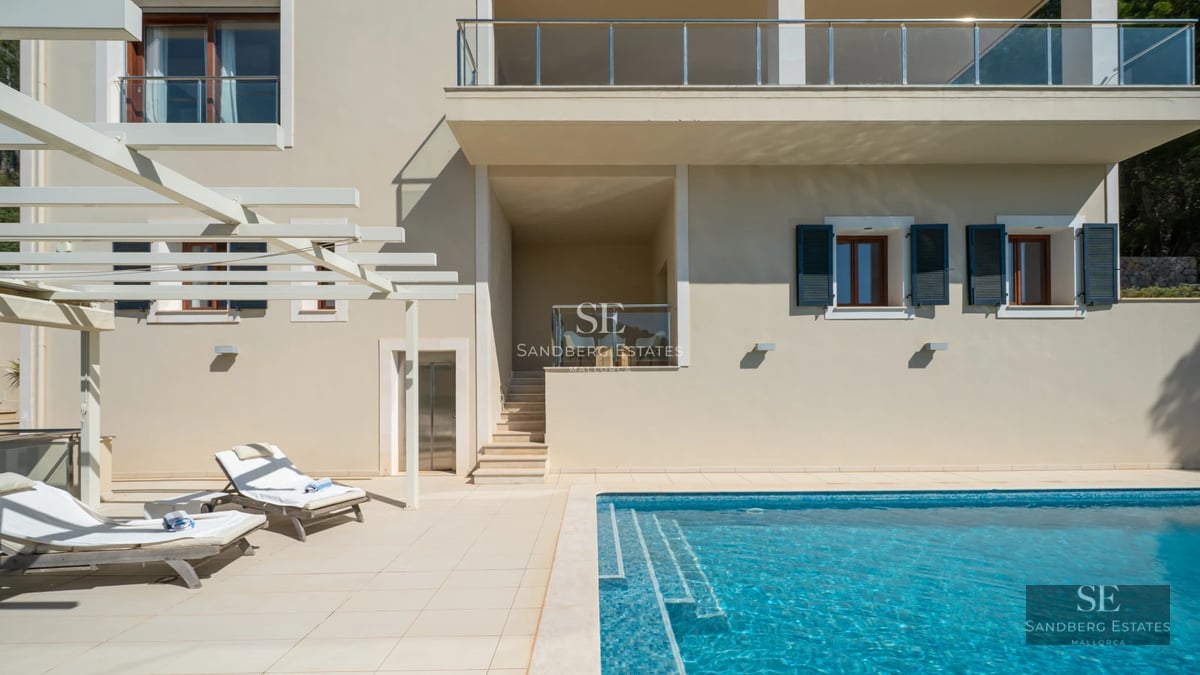 Spacious living room with floor-to-ceiling windows, light wood floors, designer sofas, and direct access to the terrace and pool.