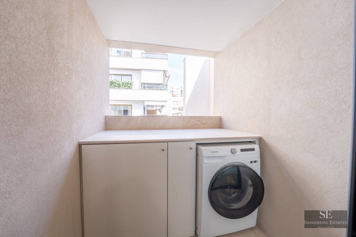 Modern washing machine and white cabinets in a textured beige balcony nook overlooking city buildings.