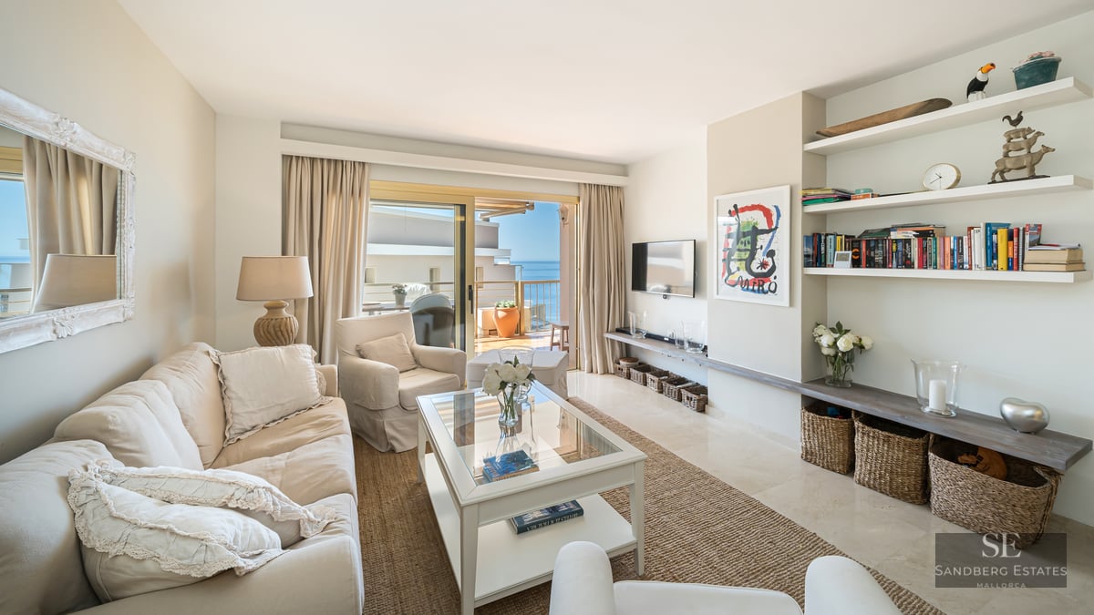 Mediterranean style living room with beige sofas, glass table, and sliding doors opening to a terrace with sea views.
