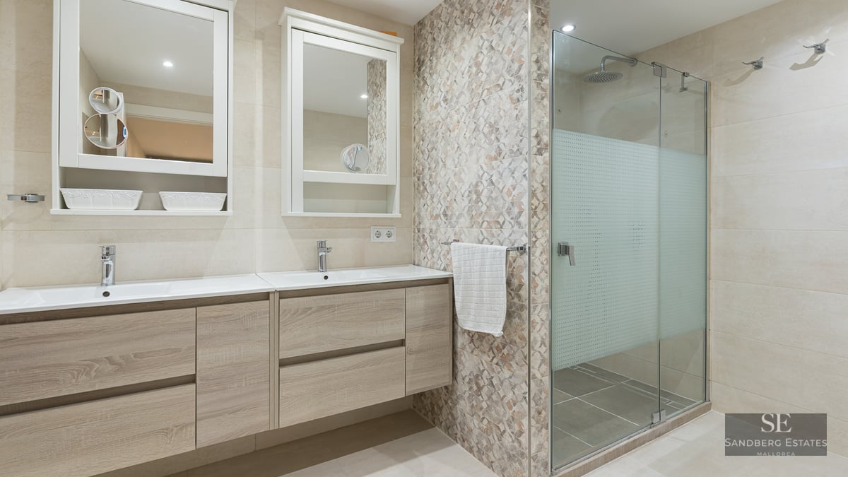 Bright master bathroom featuring a light wood double vanity, two mirrors, and a glass-enclosed walk-in shower.