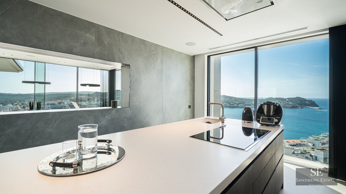 Modern kitchen island with induction hob and sea view through large floor-to-ceiling windows.