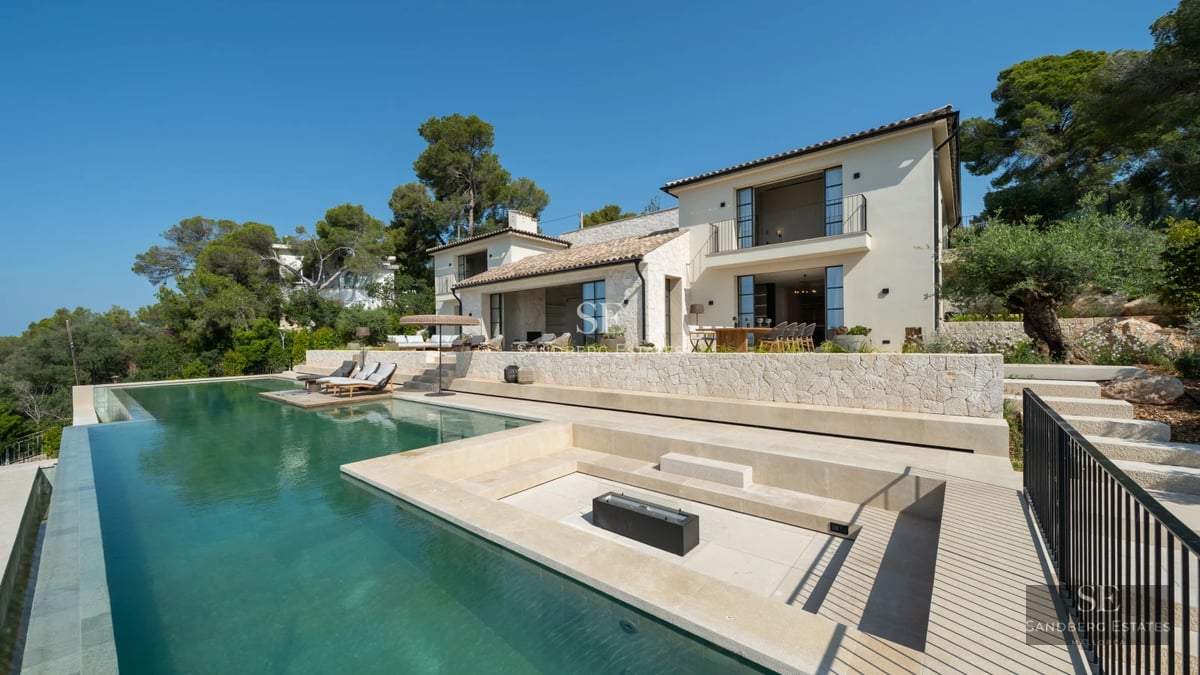 Pool view with sun loungers and lush greenery. Modern architecture with large glass windows. Natural light and relaxing atmosphere.