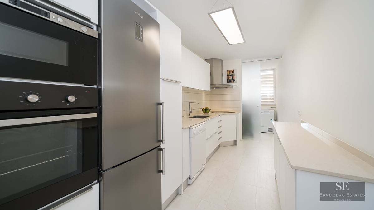 A modern galley-style kitchen with white cabinetry and stainless steel appliances.