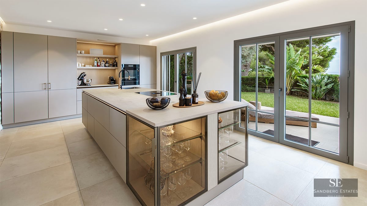 Modern kitchen featuring a large island with integrated glass displays and glass doors opening to a green garden.