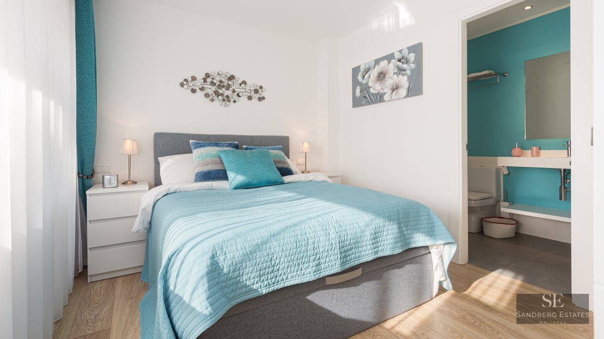 Chambre lumineuse avec lit turquoise, tête de lit grise et salle de bain privative visible en arrière-plan.