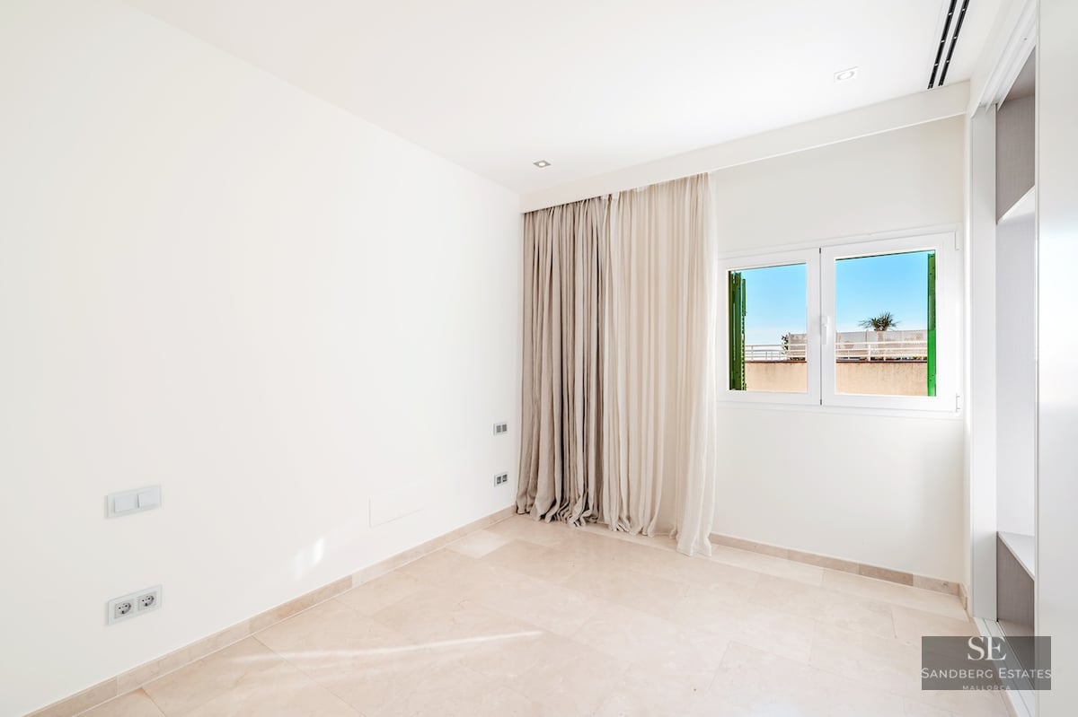 Empty bright room with white walls, polished beige stone floors, a large window with floor-to-ceiling curtains.