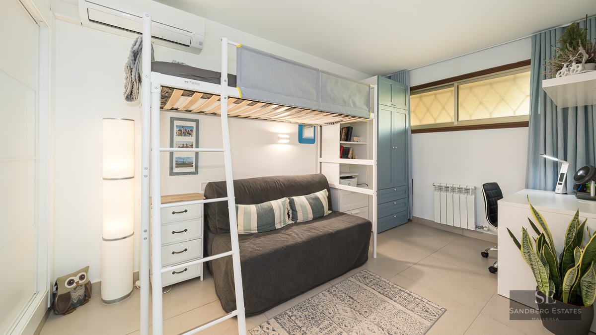 Lit mezzanine en métal blanc au-dessus d'un canapé gris, à côté d'un bureau et d'une armoire bleue.