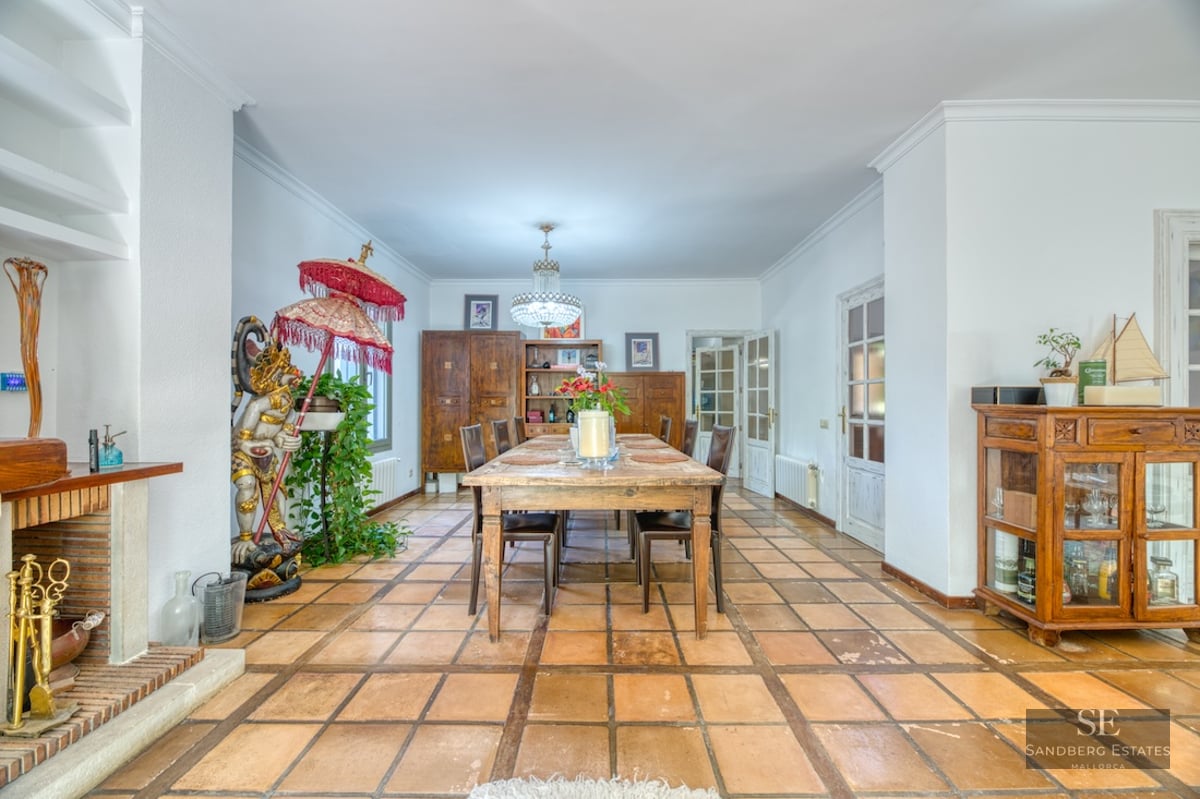 Spacious dining room featuring a wooden table, terracotta tile flooring, a fireplace, and an eclectic decorative statue.