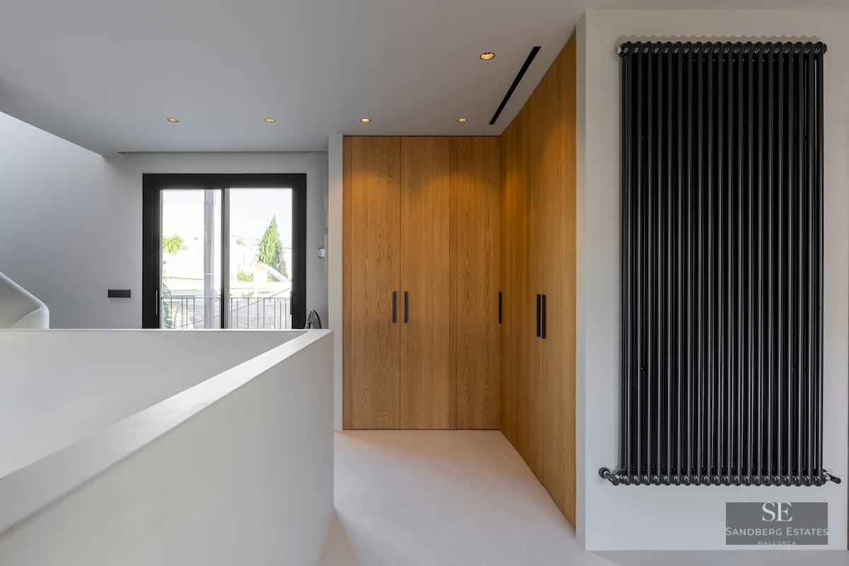 Couloir avec armoires en bois du sol au plafond, radiateur noir vertical et porte vitrée menant au balcon.