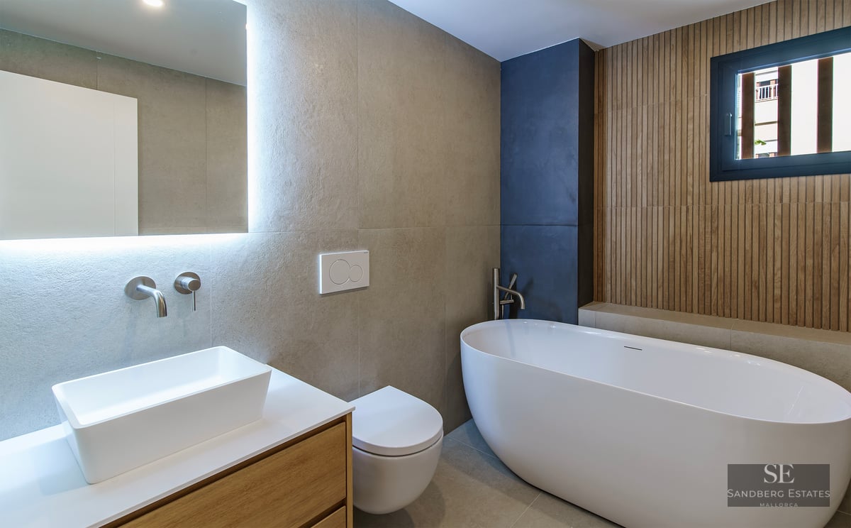 Salle de bain moderne avec baignoire îlot, vasque sur meuble en bois et miroir rétroéclairé.