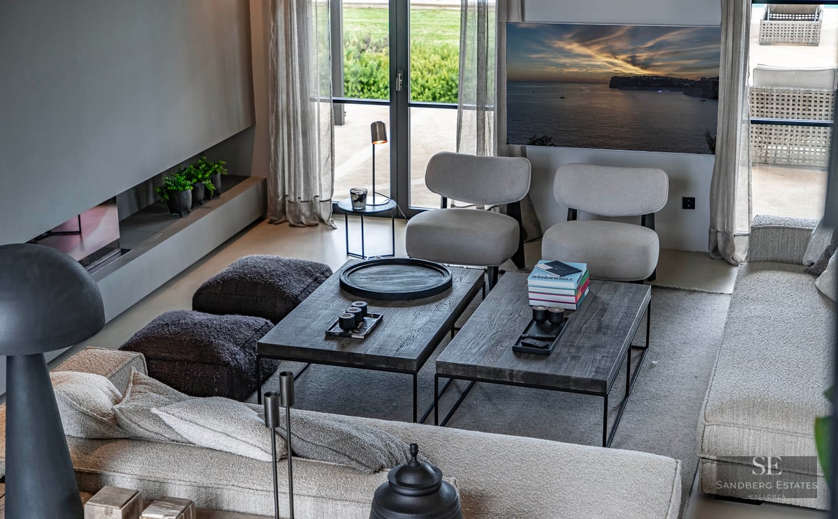 High-angle view of a luxury living room with grey seating, dark wood coffee tables, linear fireplace, and garden window.