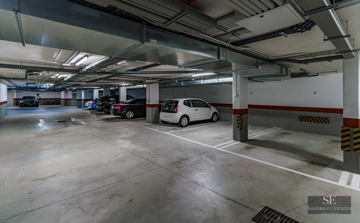 Well-lit underground parking garage with numbered stalls, parked cars, and overhead ventilation ducts.