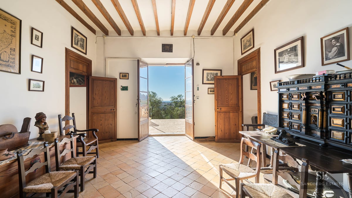 Traditional hallway with wooden beams, terracotta floors, and open doors leading to a sunny terrace.