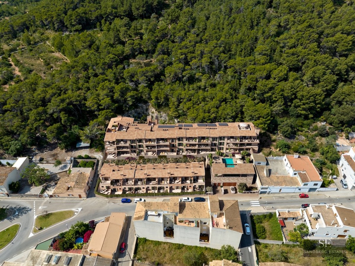 Drone shot of a Mediterranean-style apartment complex with terracotta roofs nestled against a dense green forest.