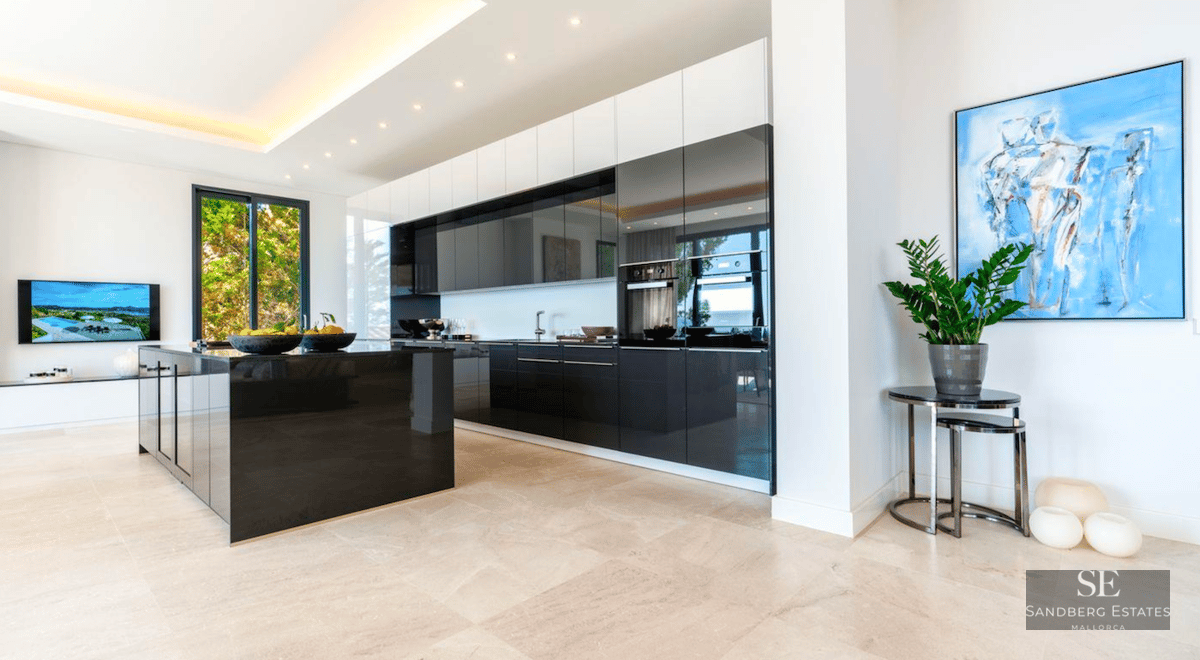 Spacious modern kitchen featuring a large black glossy island, dark cabinetry, and light stone flooring.