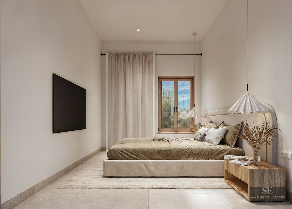 A minimalist bedroom with an upholstered bed, wooden side table, pendant lights, and natural light from a window.
