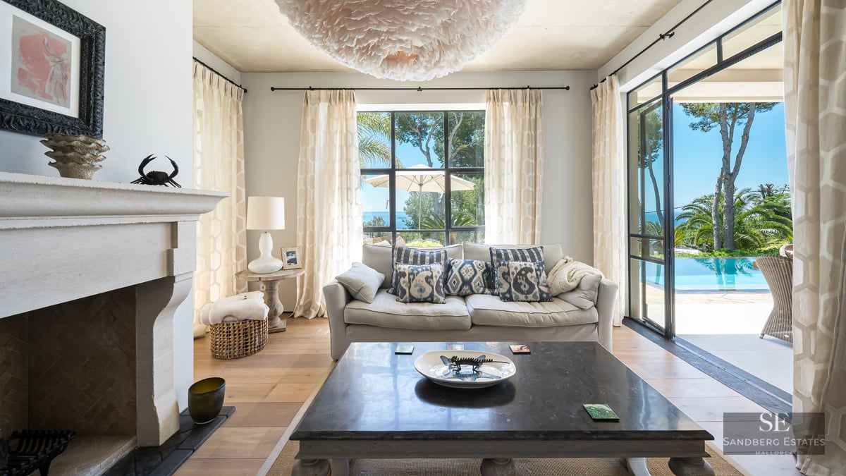 Bright living room with a stone fireplace, plush sofa, and large glass doors opening to a turquoise swimming pool.